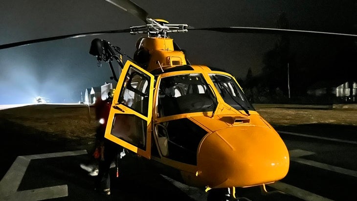 A helicopter waits at night on a tarmac before flying in to rescue climbers.