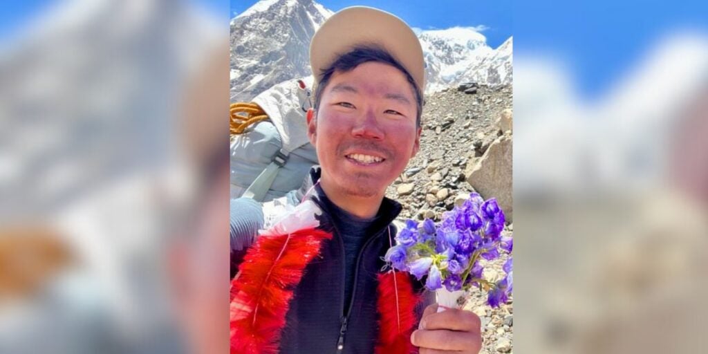 Kenro Nakajima smiles in a mountainous valley holding flowers.