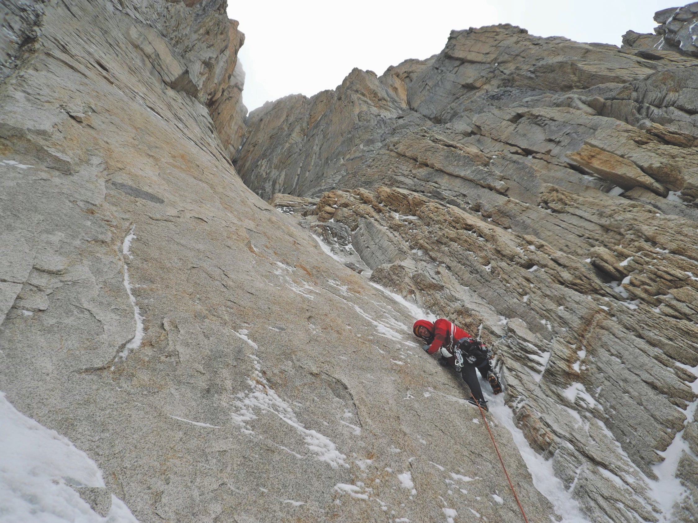 Zack Smith, a contributor to Climbing Self-Rescue, climbing a snowy and severe-looking granite cliff in Alaska.